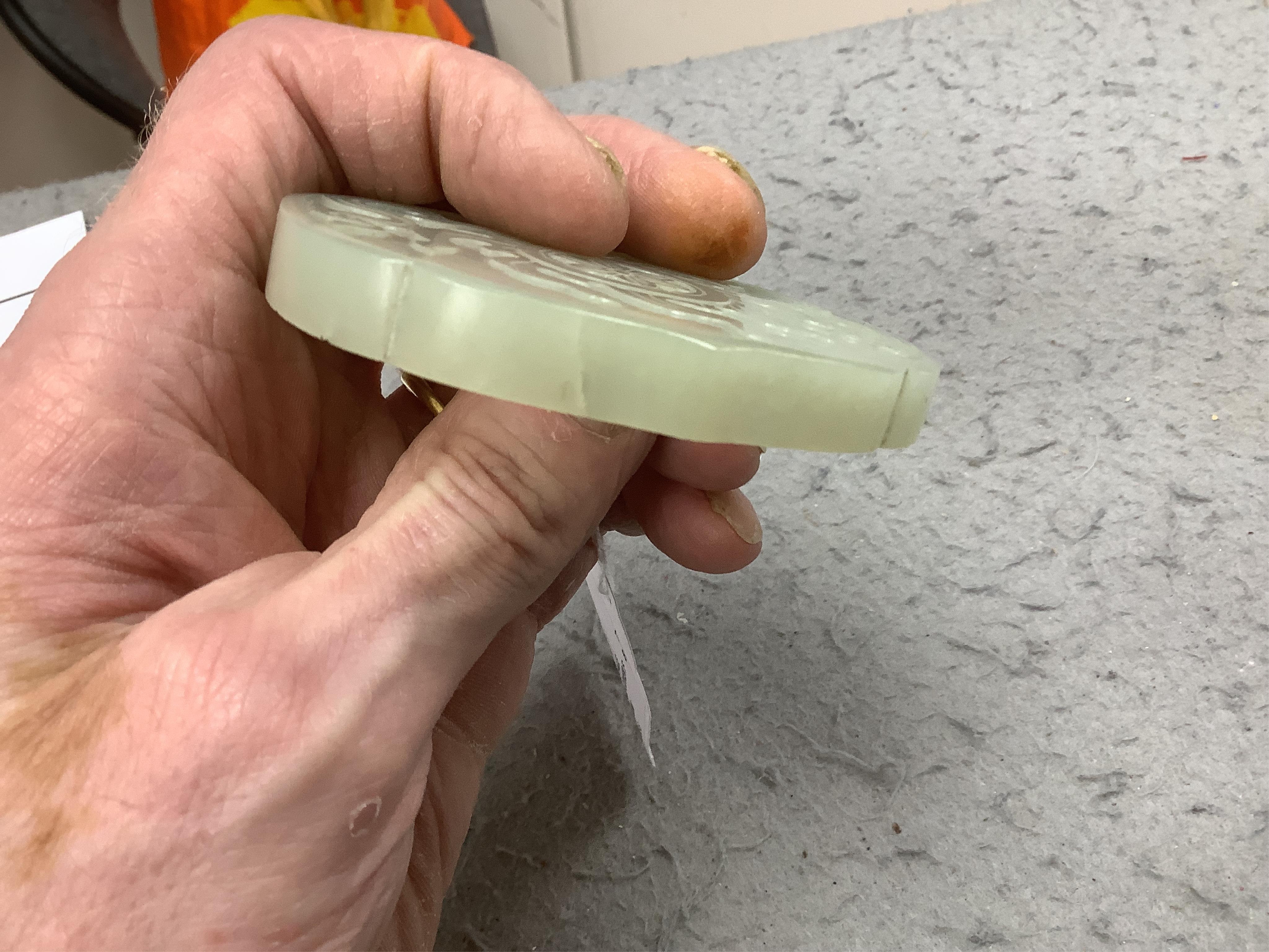 A Chinese pale celadon jade cover for a box, 19th century, carved in relief with a flaming Buddhist wheel emblem, 7.5cm wide. Condition - box base lacking, cover with feint crack